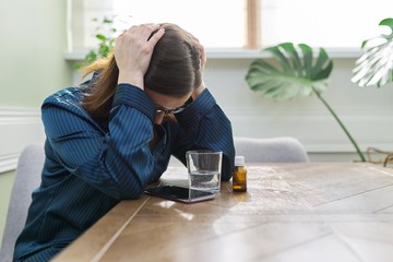 Mature woman dripping drops with glass of water, drinking sedative medicine