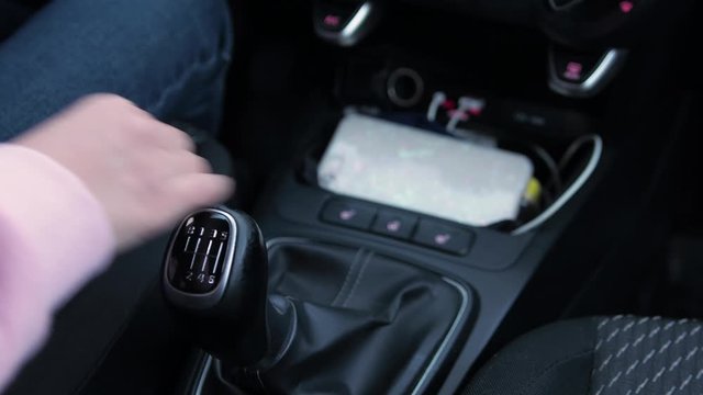Girl's hand in pink pite shifts a manual gearbox in a car.