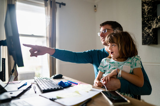 Happy father and daughter pointing at computer screen smiling while on a virtual video chat at home