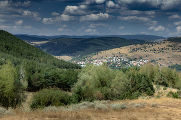 Valley landscape with village in the background surrounded by peaks and forests with blue sky and white clouds