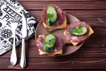 Sandwiches with meat and cheese and green cucumber on a wooden background