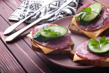 Sandwiches with meat and cheese and green cucumber on a wooden background