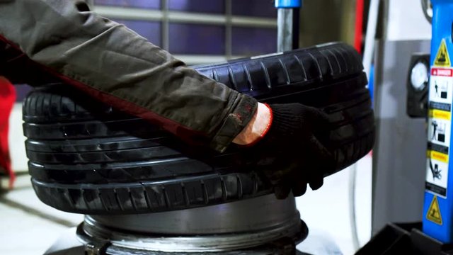 Close up of worker hands changing tire at the car service. Car mechanic is changing a tyre in a garage with the professional equipment.