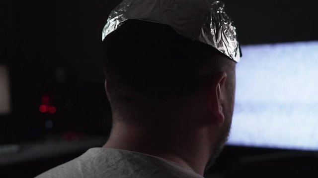 Man in tin foil hat watching white noise on TV screens at home. Orbit shot