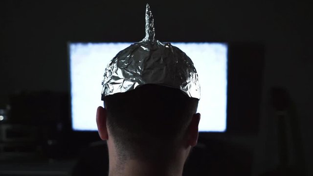 Man in tin foil hat watching white noise on TV screens at home.