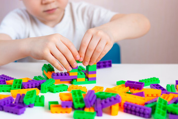 A child plays with a bright constructor on a white table. The development of fine motor skills of the hands. Quarantined home leisure.