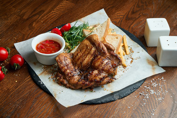 Juicy and mouth-watering grilled ribeye steak with spicy butter on a black tray with a side dish of vegetables. American cuisine.. Close up. Wooden background