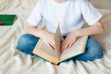 Obraz premium The child sits on the bed and holds an open book on his lap. Home leisure - reading a book.