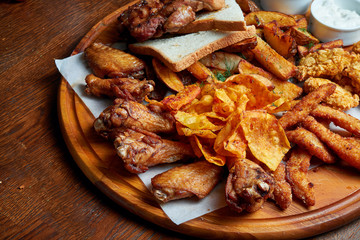 An excellent beer snack is a set of chicken nuggets fries with parchment sauce on a stone tray. Pub food. Close up.