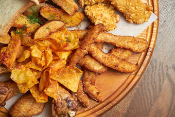 An excellent beer snack is a set of chicken nuggets fries with parchment sauce on a stone tray. Pub food. Close up.