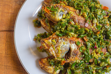 Ikan nila cabe hijau is indonesian food. made from fish, green chilies, garlic and other ingredients. has a savory and spicy taste. on white plate