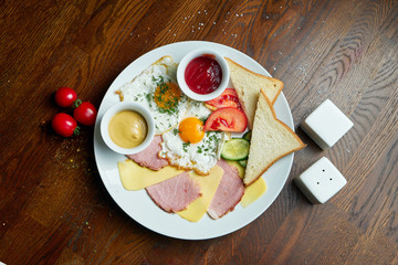 Classic English breakfast: toasts, smoked sausages, fried eggs, potato and fried toasts on a white plate on wooden background
