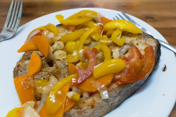 A piece of fried fish with peppers, tomatoes and onions on a plate with sauce