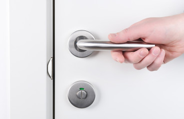 Hand holding doorknob, opening or closing the door, with bright behind the door.Hand holds door handle.