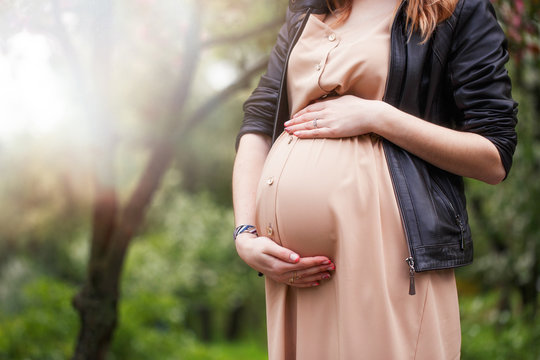 Pregnant woman wearing beige dress and black coat standing near blossoming tree in spring. closeup. cropped image