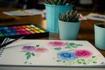 Close-up watercolor roses painting surrounded by cactuses and a watercolor palette