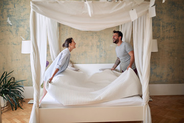 Couple making bed.Charming man and woman in love making bed together.
