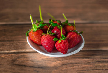varias fresas con hojas y tallos verdes en un plato plano sobre una tabla de madera