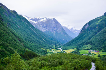 The road running in valley between high mountains with snowy peaks in which Glaciers of Jostedalsbreen National Park is located.