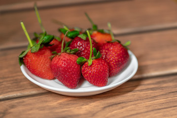 fresas rojas con tallos y hojas verdes en plato plano sobre una madera