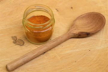 Fototapeta na wymiar Turmeric powder (Curcuma longa) on a wooden spoon and glass pot on wooden board.