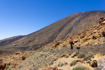 Empty road by Teide mountain arid slope. Dry landscape with cable cars heading up to popular volcano on background. National park in Tenerife island, Spain. Holidays travel destination concept