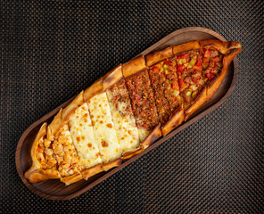 turkish pide with stuffed meat, cheese and pieces of chicken on a wooden bowl