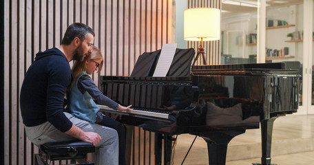 Dad teaching piano to his daughter.Little girl learning piano at home.Side view.Piano class at home. Child learning piano from her father