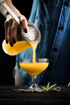 bartender pours orange cocktail from the shaker