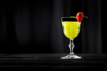 Gin Basil Smash, green cocktail on black wooden bar with black background