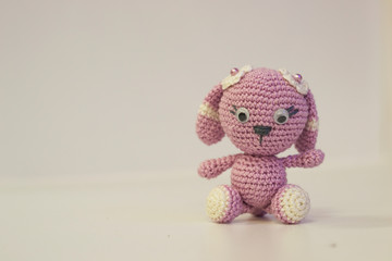 Amigurumi hare of pink color, sitting on a white background. Needlework concept.