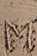 the letter m written in beach sand
