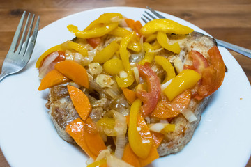 A piece of fried fish with peppers, tomatoes and onions on a plate with sauce