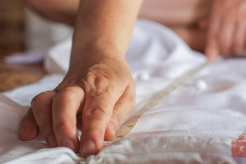 Hand of seamstress is using a tape measure to measure the size of the white shirt close-up.