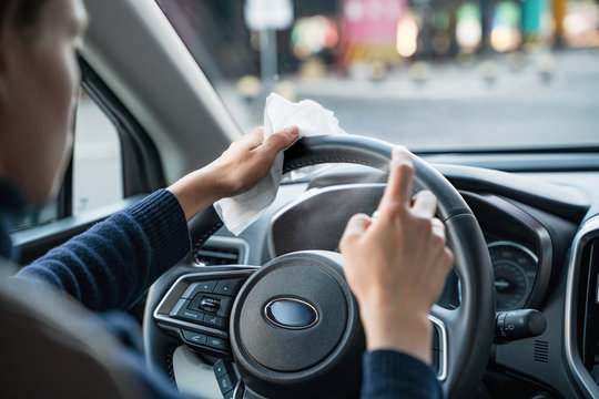 Hands of woman uses disinfectant spray on steering wheel in her car