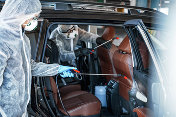 Disinfectant worker in protective masks and suits making disinfection of car seats
