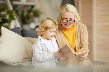Grandmother in eyeglasses reading a book to her son during their leisure time at home