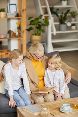 Grandmother reading a book to her grandchildren while they sitting on sofa in the living room