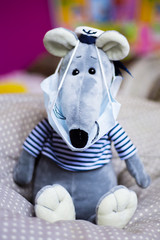 close up of a toy mouse in a medical mask sitting at home on a grey pillow with dots in sailors hat...