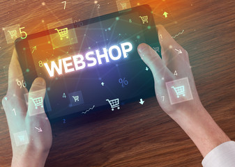 Close-up of a hand holding tablet with WEBSHOP inscription, online shopping concept