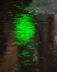 Rainy day. A puddle with raindrops and reflections of a green lantern pharmacy in a puddle. City landscape, street photography