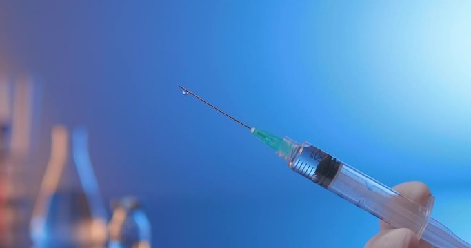 Removing air from syringe filled with vaccine. Close-up side shot on a blue laboratory background.