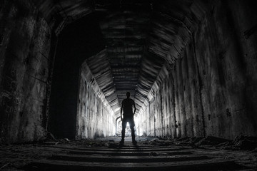 Shilouette of human underground explorer in abandoned dark tunnel with light in the end.
