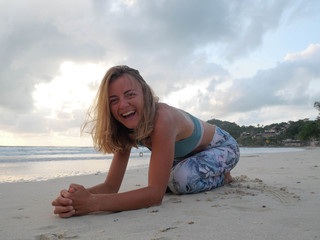 Fototapeta na wymiar Young smiling caucasian girl in sportswear practice yoga at seaside