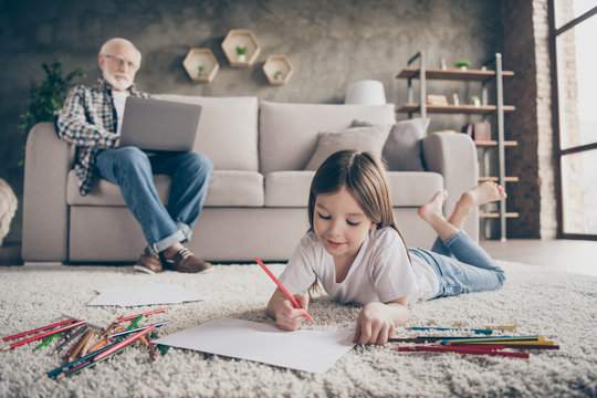 Photo of two people grandpa working online browsing laptop little granddaughter lying floor carpet painting colorful pencils stay home quarantine living room indoors