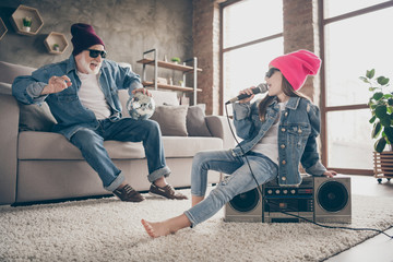 Photo of two people grandpa fan listen little granddaughter sing mic old fashion song cool style specs denim outfit hat house party sit tape player recorder stay home quarantine indoors