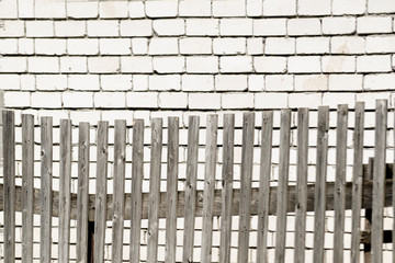 Old grey boardwalk wooden fence with parallel planks in front of a white brick wall on a bright sunny day. A concept of rural life with space for text