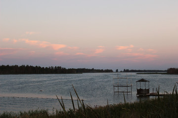 Pink-blue sunset on the sky with clouds over the lake by the sea bay with waves