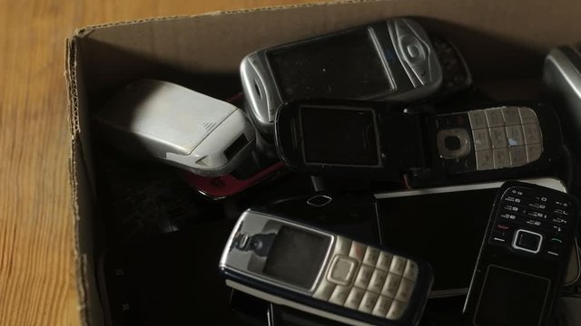 Outdated cell phones are in a big pile in a cardboard box. Old broken scratched mobile devices are recycled. analog communication.