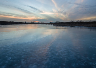 Pastel colors of a winter sunset reflected in the frozen surface of a frozen pond.